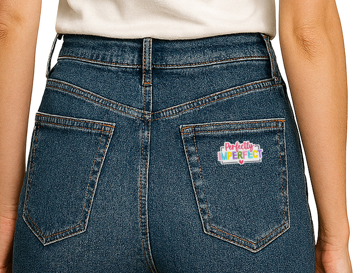Back view of blue denim jeans featuring a "Perfectly Imperfect" colorful embroidered patch on the right back pocket, showing a creative way to customize clothing.