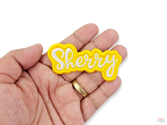 Yellow embroidered name patch with 'Sherry' text held in a hand to show scale, texture, and detail of the embroidery.