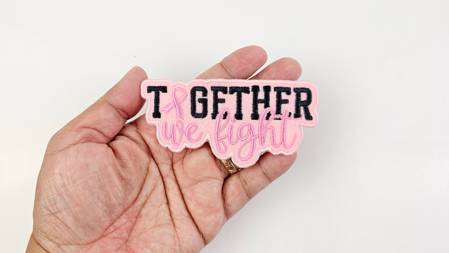 Hand holding a pink and black patch with 'Together we fight' text on a light pink background
