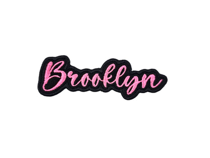 Brooklyn custom name patch by Shirts Patches And More, embroidered in pink script with a black border on a white background.
