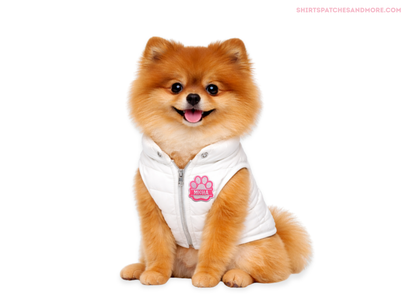 Small Pomeranian dog wearing a white quilted vest with a custom pink and white embroidered paw print name patch featuring the name 'Micha' on a white background.