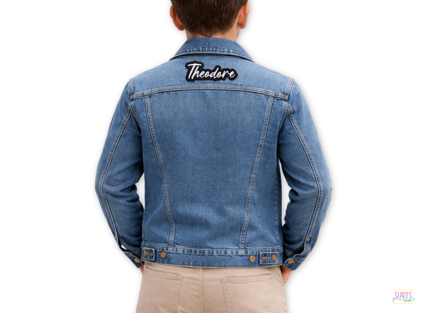 A blue denim jacket with a custom 'Theodore' embroidered name patch featuring white script text on a black background, centered on the upper back.