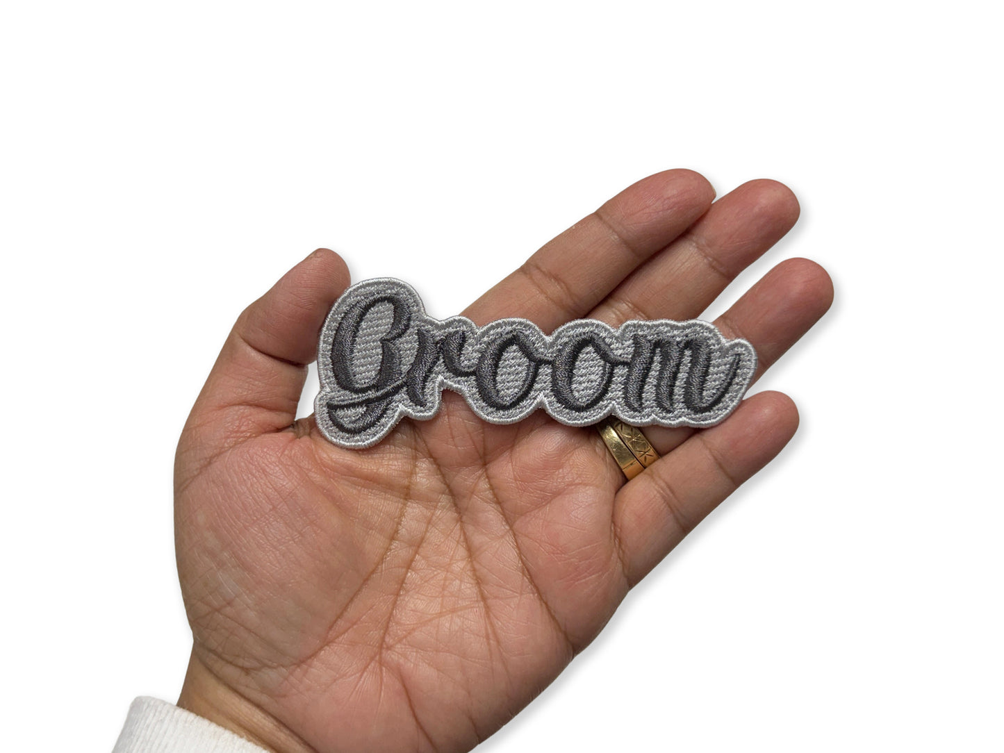 Hand holding a 'Groom' embroidered patch on a white background