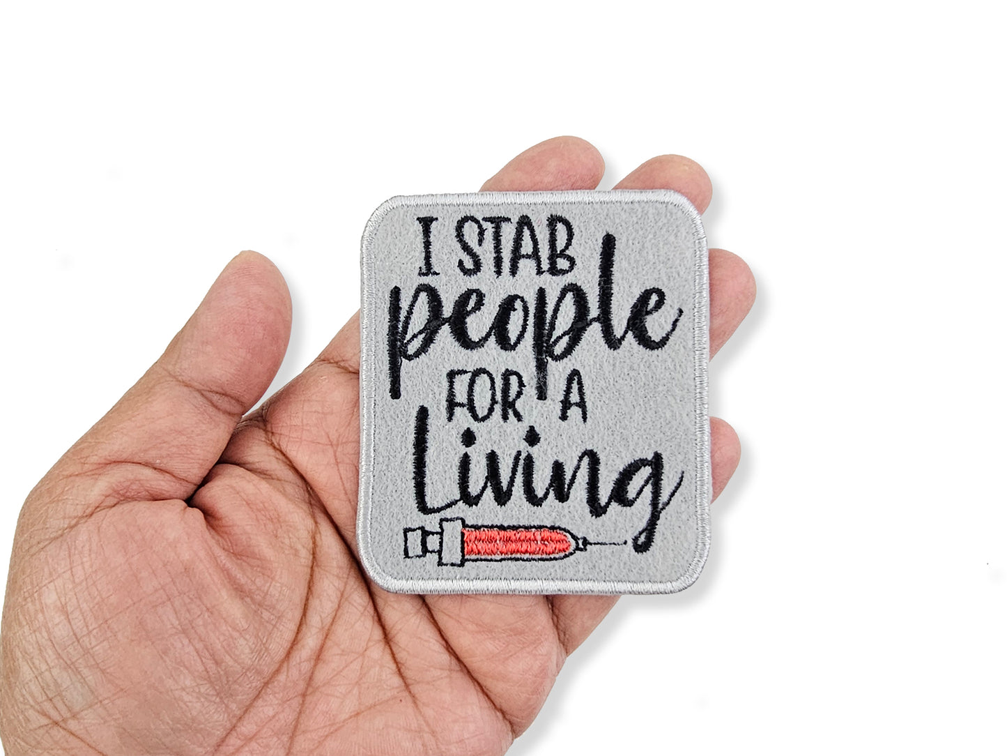Patch with 'I stab people for a living' text held in a hand on a white background