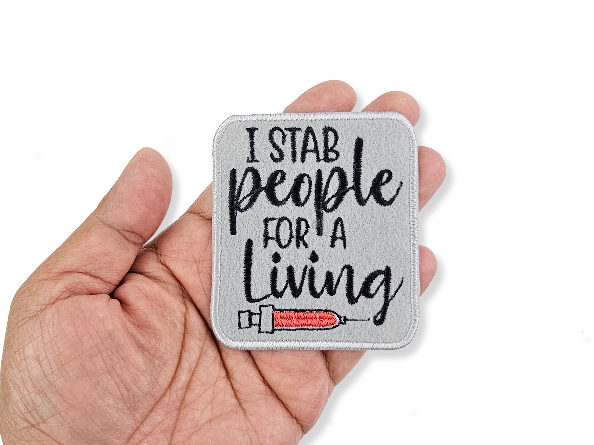 Patch with 'I stab people for a living' text held in a hand on a white background