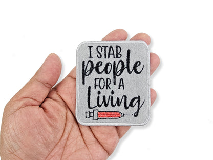 Patch with 'I stab people for a living' text held in a hand on a white background