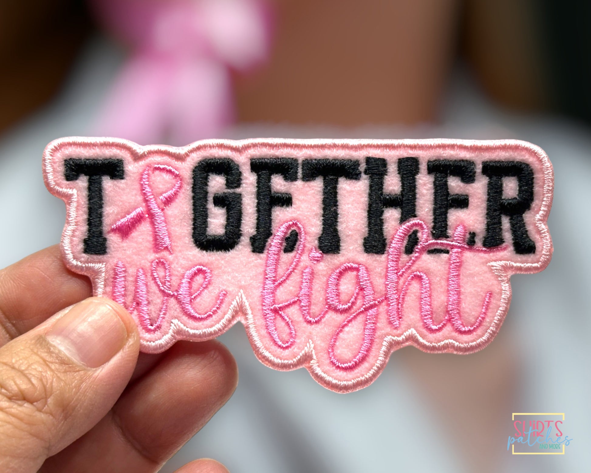 Patch with 'Together we fight' text held by a hand, with a pink ribbon symbol.