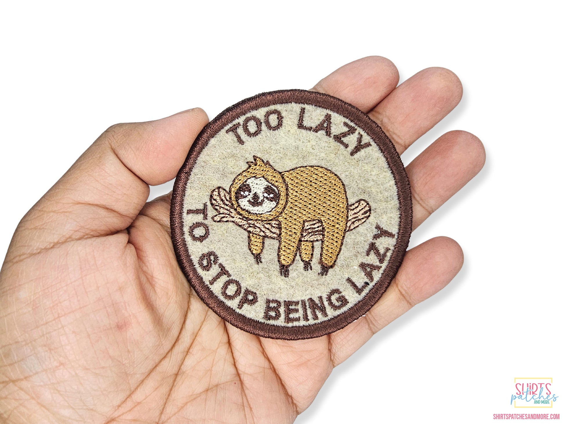 Hand holding a 3-inch "Too Lazy to Stop Being Lazy" sloth patch, showing the high-quality embroidery detail and scale against a person's palm.