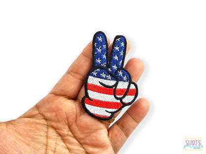 Hand holding a patriotic peace sign patch with an American flag stars and stripes design to show scale against a white background.