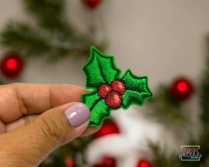 Close-up of the embroidered holly patch held between fingers showing stitch detail