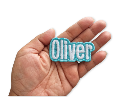 Oliver custom embroidered name patch with light aqua blue border, held in an open hand to show size and texture.