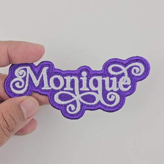 Video showcasing the Monique custom embroidered patch, held in hand, highlighting the white script on a purple background.