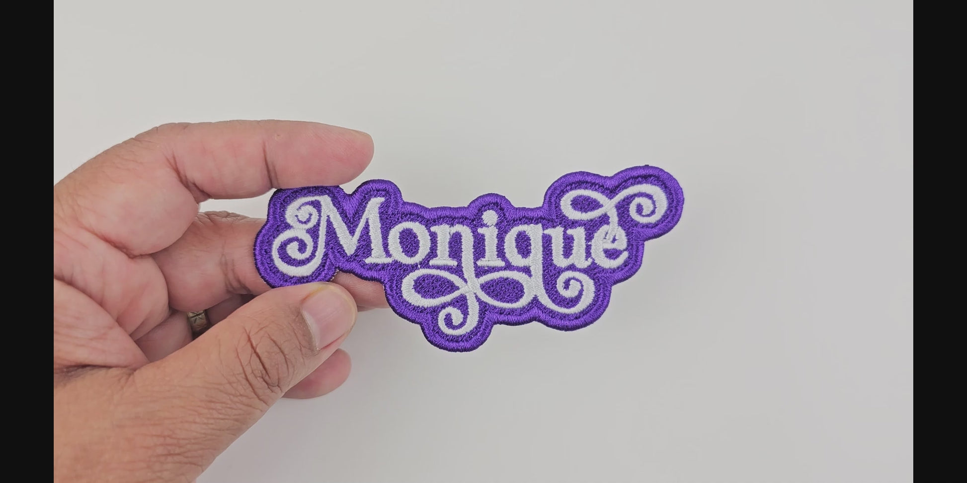 Video showcasing the Monique custom embroidered patch, held in hand, highlighting the white script on a purple background.