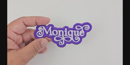 Video showcasing the Monique custom embroidered patch, held in hand, highlighting the white script on a purple background.