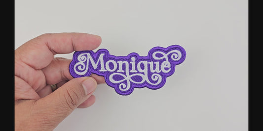 Video showcasing the Monique custom embroidered patch, held in hand, highlighting the white script on a purple background.
