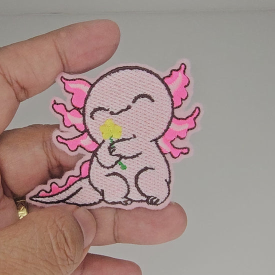 Video clip of a hand holding the cute pink axolotl embroidered patch to demonstrate size and stitching quality.