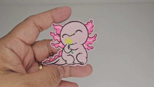 Video clip of a hand holding the cute pink axolotl embroidered patch to demonstrate size and stitching quality.