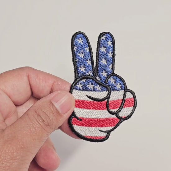 Video demonstration of a hand-embroidered peace sign patch featuring a patriotic red, white, and blue American flag design with stars and stripes.