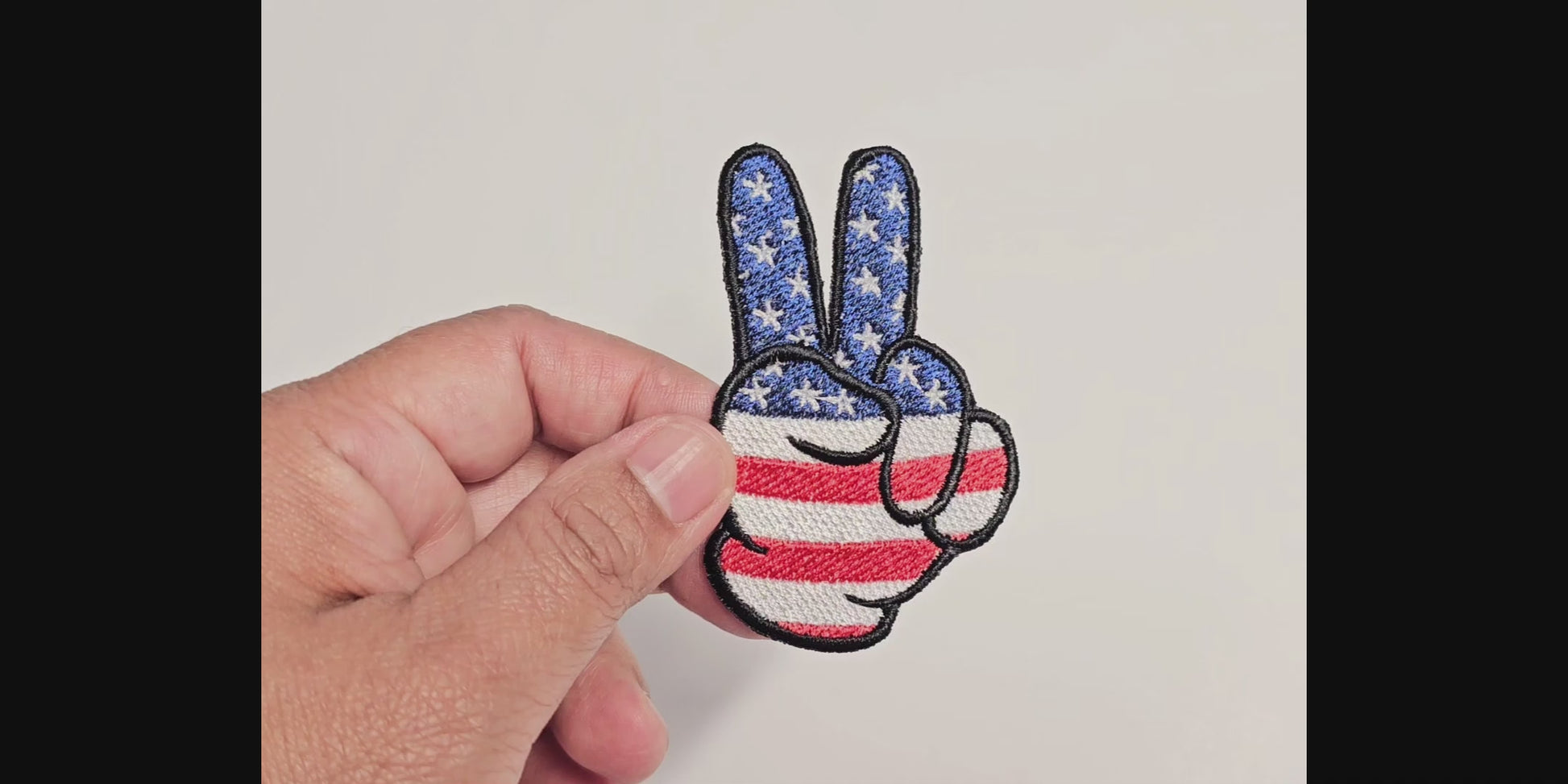 Video demonstration of a hand-embroidered peace sign patch featuring a patriotic red, white, and blue American flag design with stars and stripes.