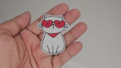 Video showing details of white cat embroidered patch with red heart sunglasses and scarf held in hand