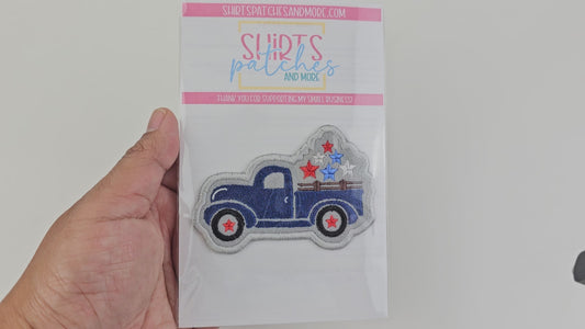 Close-up video of a blue vintage truck patch with patriotic stars, displayed in its official Shirts Patches and More retail packaging with a pink and white branded header card.
