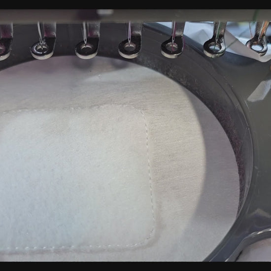 A close-up video of a white embroidered patch being made on an industrial machine, featuring a unicorn  and "God Bless The USA" text in pink and purple.