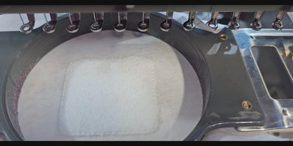 A close-up video of a white embroidered patch being made on an industrial machine, featuring a unicorn  and "God Bless The USA" text in pink and purple.