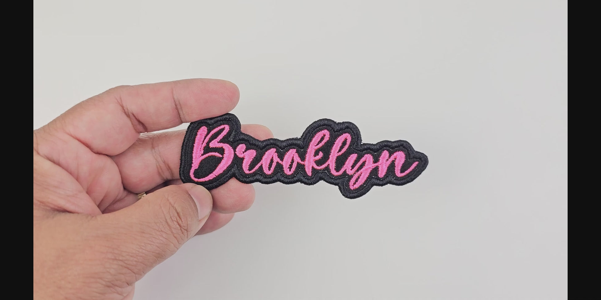 Video showcasing the Brooklyn custom embroidered patch, held in hand, highlighting the pink script and black border.