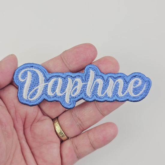 Close-up video of a hand holding the blue and white Daphne custom embroidered name patch, showing the texture and quality.