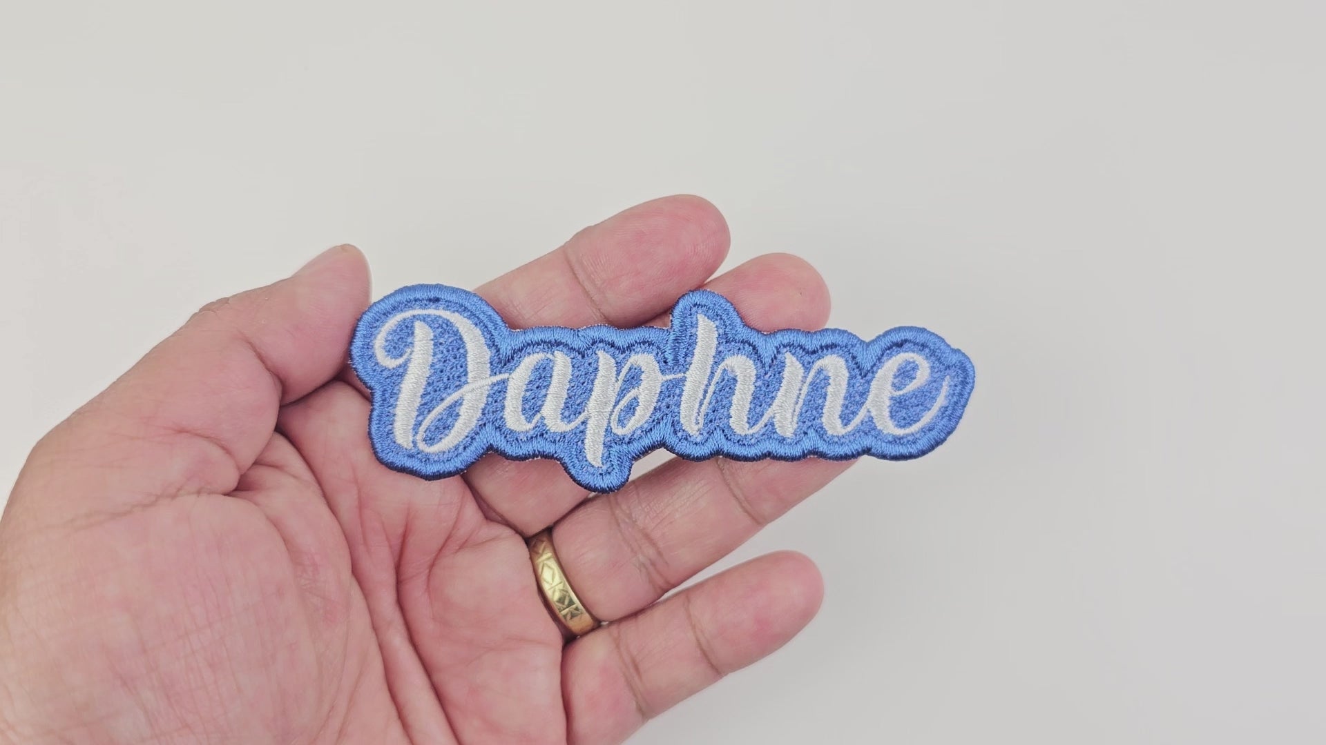 Close-up video of a hand holding the blue and white Daphne custom embroidered name patch, showing the texture and quality.