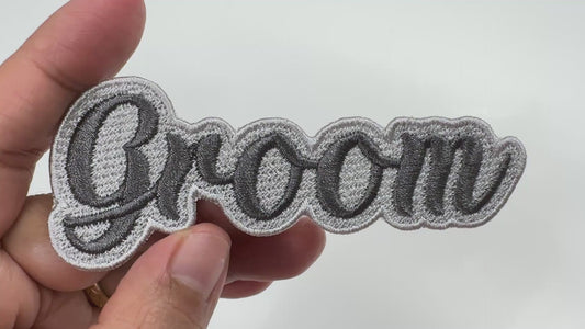 Handheld video showing a high-quality 'Groom' embroidered patch with dark grey script lettering and a light grey bordered edge, demonstrating the detailed stitching.