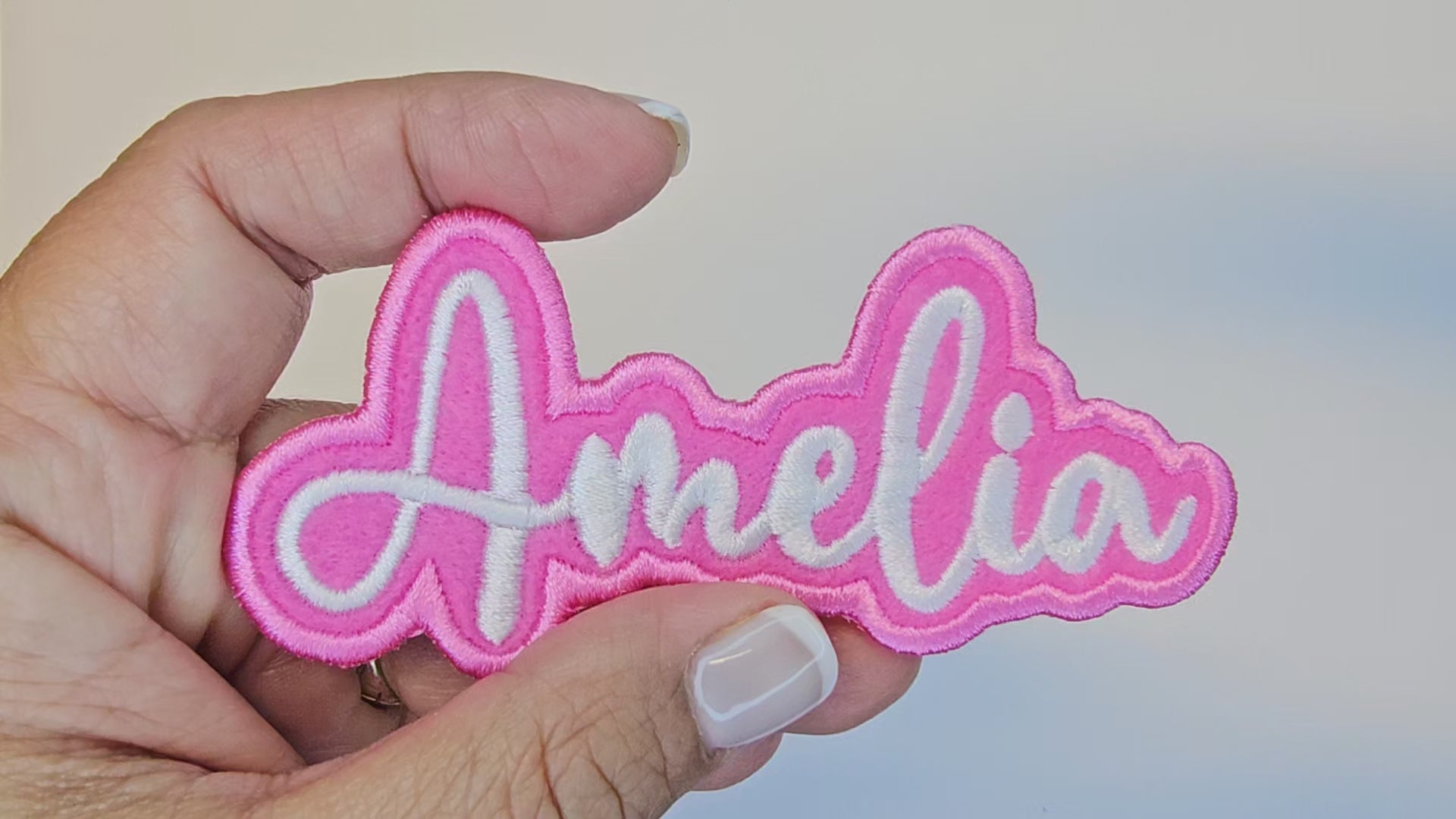 Video showing a close-up of the Amelia embroidered name patch held in hand and rotated to display stitching and details.