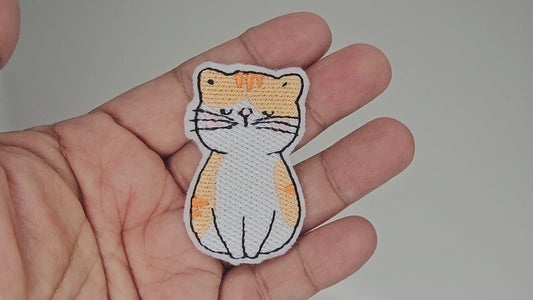 Video of hand holding a white and orange tabby cat embroidered patch to show size and quality