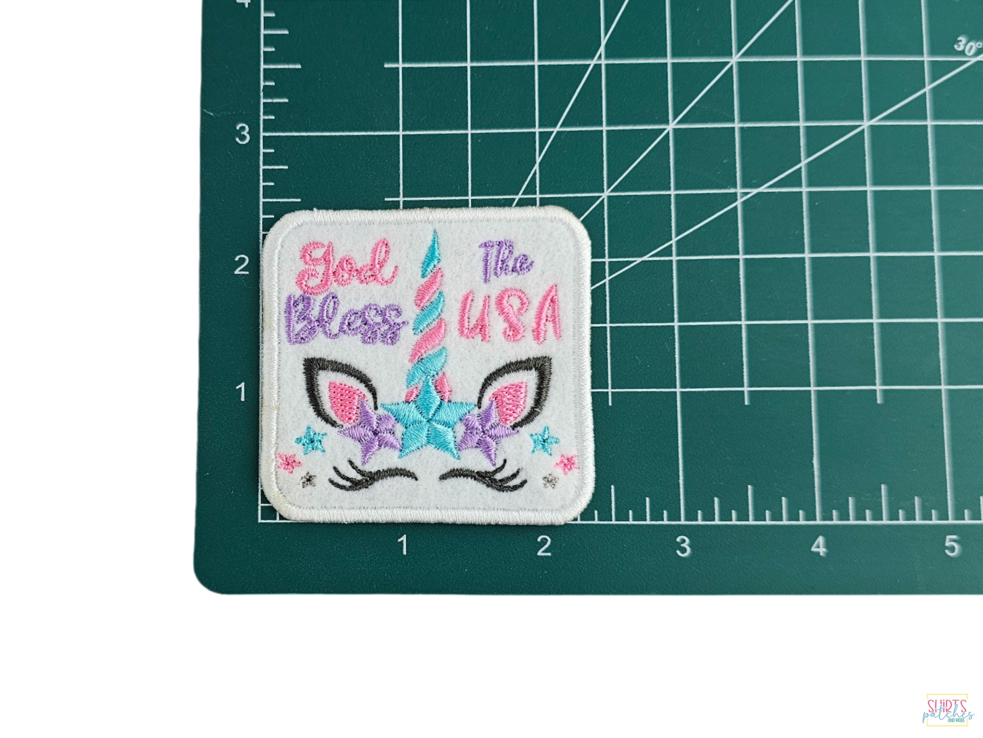 God Bless The USA unicorn embroidered patch shown on a measuring mat to demonstrate its 2.5-inch size.